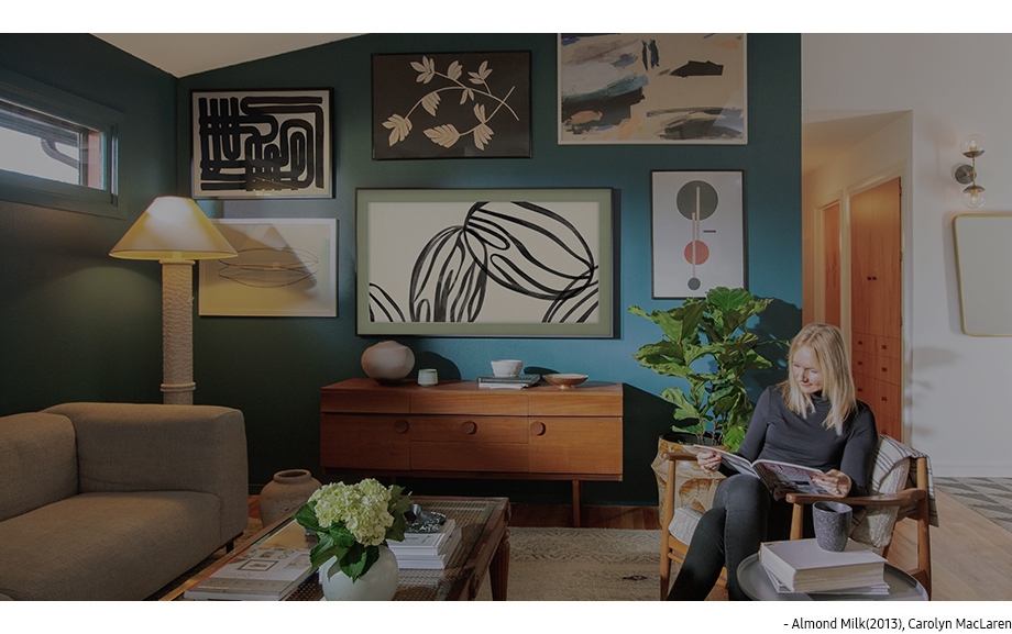 Various artworks, including Almond Milk (2013) by Carolyn MacLaren displayed on The Frame, hang on the living room wall in Kirsten Grove's home.