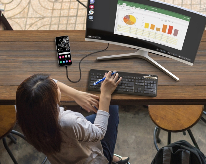 A birds-eye view of a lady sitting at a desk and using Samsung’s DeX Station to make working remotely a breeze