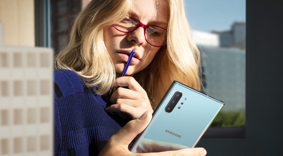 A lady holding an S Pen to her lips while looking at her Galaxy Note10 phone