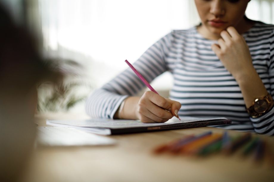A lady sitting at desk and writing something, the foreground of the shot is blurred
