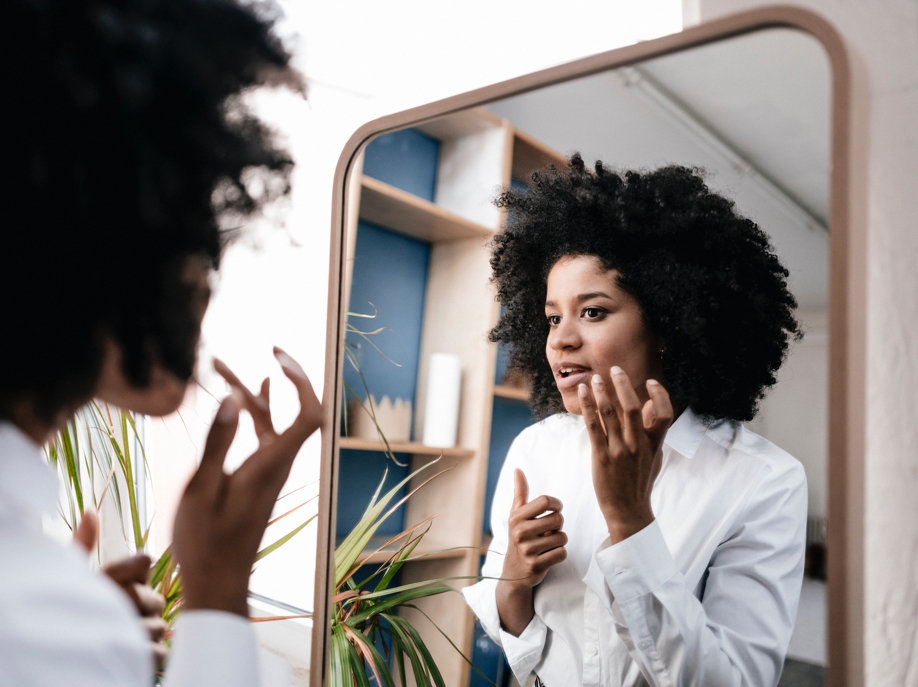 A lady looking in the mirror, she is applying something to her face