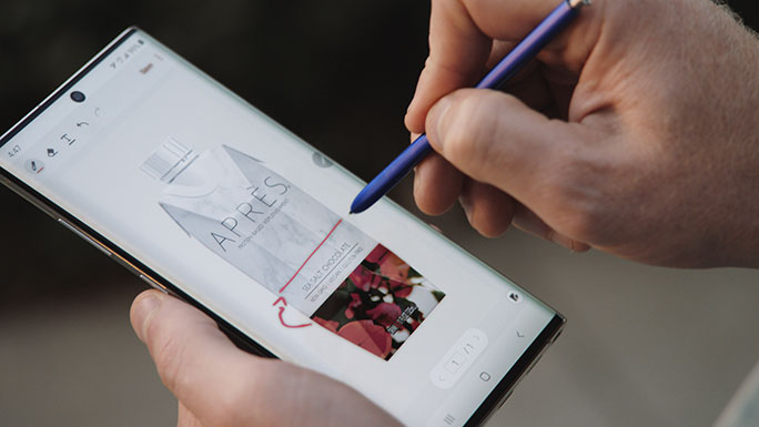 A close-up shot of a Galaxy Note10 and S Pen in Sonny McCracken’s hands. On the phone's screen you can see that he is using the S Pen to draw lines on an image of the Après protein drink's packaging.