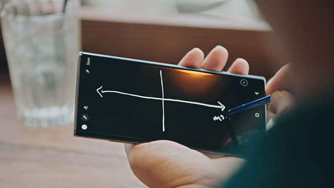 A close-up shot of a Galaxy Note10 and S Pen in Kevin Lin's hands. He is using the S Pen to draw lines and make notes on the phone's black screen.