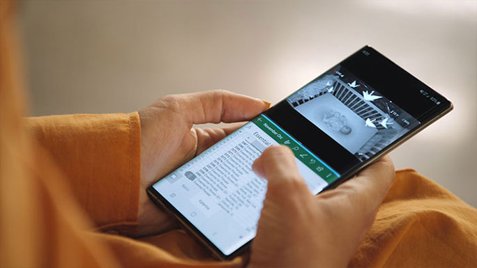 A close-up shot of a Galaxy Note10  in Katerina Schneider’s hands. You can see a photo of a baby in bed on the top half of the phone's screen and a spreadsheet document on the bottom half.