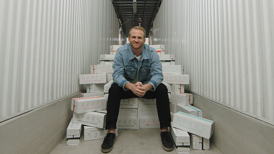 A screen grab of a video  showing entrepreneur Sonny McCracken sitting on a pile of Aprè protein drink boxes.