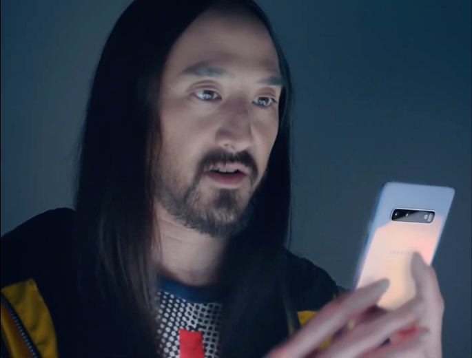 Steve Aoki holds up a prism white Galaxy S10+ and stares into the display