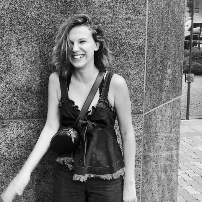 Black & white street photography shot of Millie Bobby Brown smiling in a denim top and jeans while spreading positivity