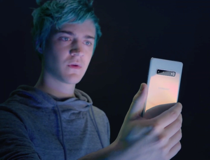 Ninja holding a prism white Galaxy S10+ smartphone in his hand as he stares at the display