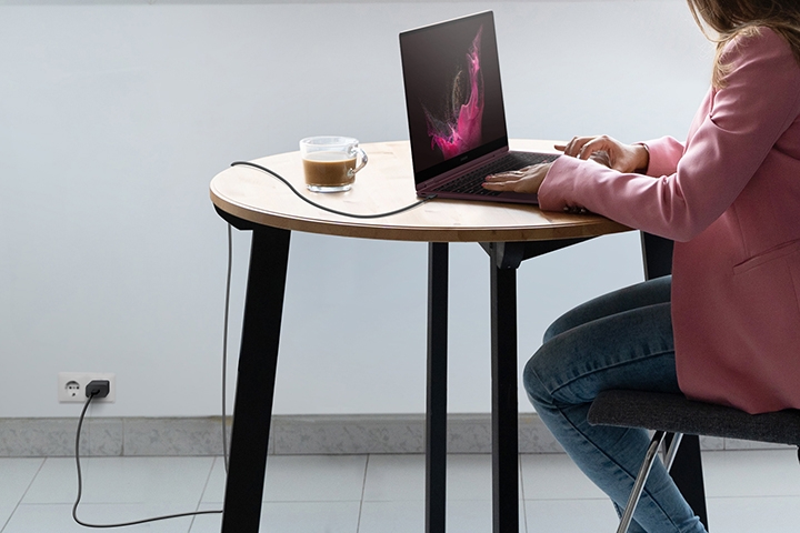 A person sitting at a table and using a Galaxy Book laptop. The USB cable is plugged in to the …