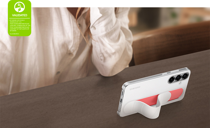 A Galaxy S25+, installed with the Standing Grip Case in White, stands in a slanted angle. It is being used for watching videos in horizontal mode. On the left corner, a UL Environmental Claim Validation Mark is shown that reads 'EF-GS931 CONTAINS A MINIMUM OF 7.7% POST-CONSUMER RECYCLED CONTENT, CONSISTING OF 18% POST-CONSUMER RECYCLED CONTENT IN THE PLASTIC OF EF-GS931. UL.COM/ECV'.
