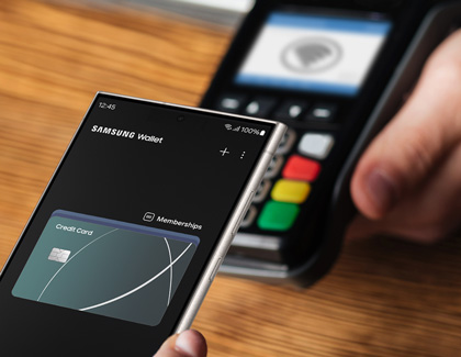 Hand holding a Galaxy phone while hovering over a point of sale terminal with the Samsung Wallet app open