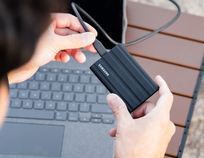 Person connecting a cable to a Samsung Portable Solid State Drive in front of a Windows laptop