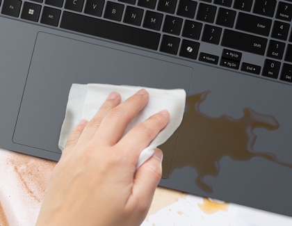 Hand wiping a wet spill on a laptop's touchpad with a cloth