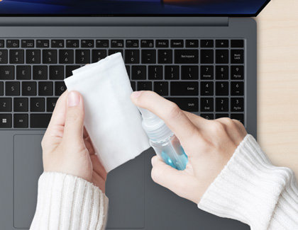 Person holding a cloth and a spray bottle, preparing to clean a laptop keyboard