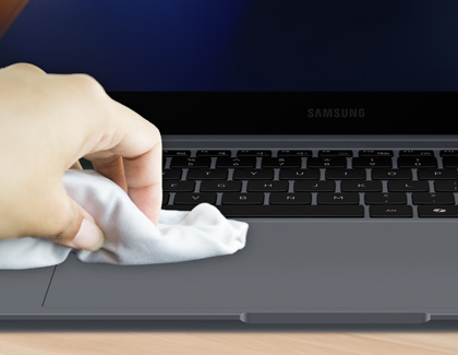 Hand using a cloth to dry clean the surface of a Samsung laptop