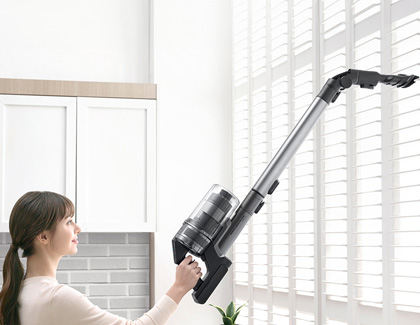 Woman using a Samsung Jet Stick vacuum to clean between the window blinds