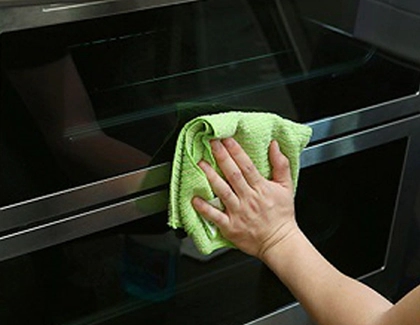 Hand holding a rag and cleaning the exterior of a Samsung oven