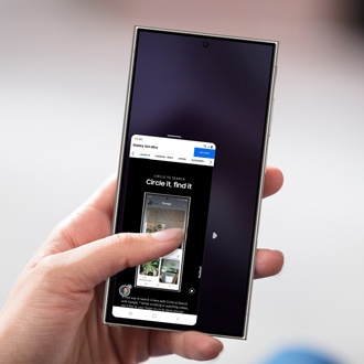 Hand holding a Galaxy phone displaying a Samsung webpage in one-handed mode, with the screen scaled down for easier access