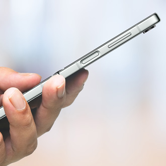 Close-up of a person's hand holding a Galaxy phone, showing the side view with the Bixby button and volume controls against a blurred background.