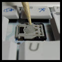 Close-up image showing a tool being used to reattach a keycap onto the plunger mechanism of a laptop keyboard, with surrounding keys visible for context.