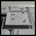 Detailed view of the underside of a laptop keycap, showing the intricate attachment points and the symbols indicating correct placement direction.