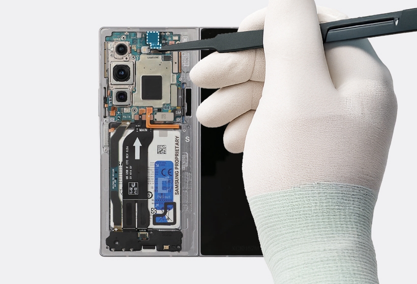 A gloved hand uses tweezers placing the front camera module into its designated hole on the Galaxy Z Fold6 main board.