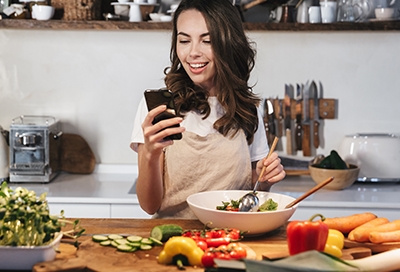 Woman making a salad while looking at phone