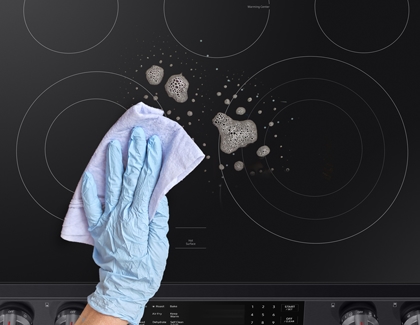 Person with gloves cleaning Samsung cooktop with glass cleaner