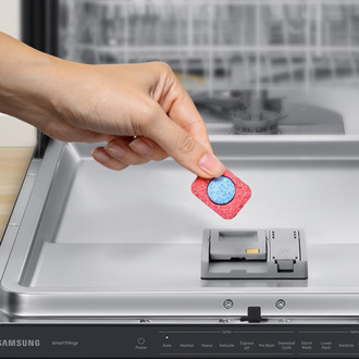 Hand holding dishwasher detergent in front of a Samsung dishwasher