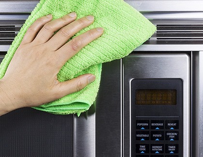 Person using microfiber cloth to clean the microwave's exterior