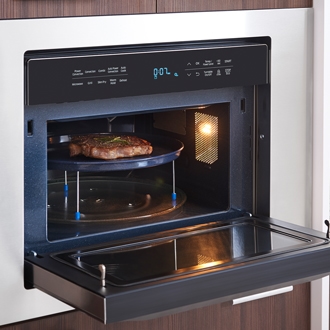 Samsung microwave oven with the door open, showing a steak being cooked on a turntable with the interior light on