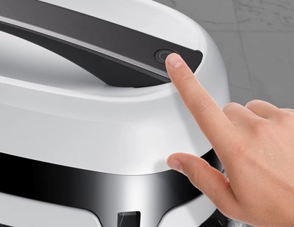 A finger pushing the Operation button on a Samsung Jetbot Mop