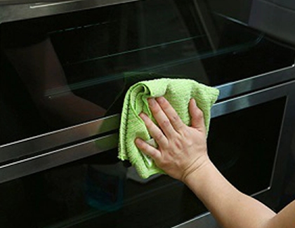 Hand wiping the outside door of the oven with a soft green dry cloth