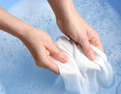 A person cleaning a white cloth in a blue tub.