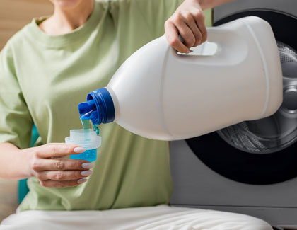 A woman pouring liquid detergent onto the cap of a detergent bottle