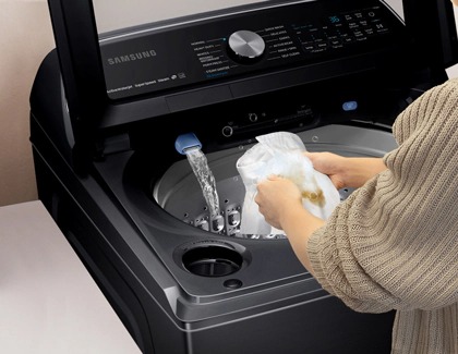 A person scrubbing a stained garment under running water in a Samsung washing machine.