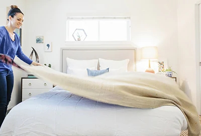 A woman spreading clean bedding onto a mattress