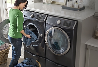 A woman in pajamas loading clothes in a Samsung washing machine.