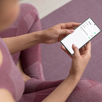 Person sitting on a yoga mat holding a Galaxy phone with the Samsung Health app open