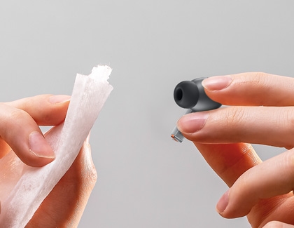 A person's hand holding a cleaning cloth while cleaning a Galaxy Buds3 Pro earbud.