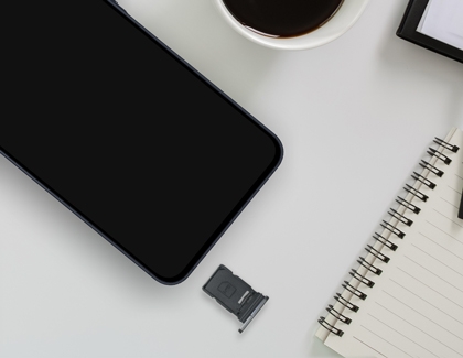 A top down view of a dark blue Galaxy A57 on a white desk with its SIM card tray removed and placed