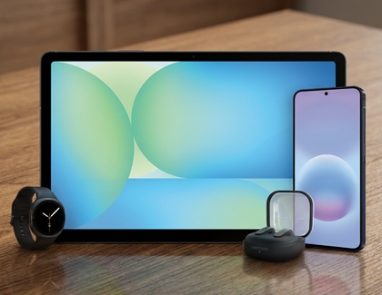 A Galaxy A series phone shown next to a Galaxy tablet, a Galaxy Watch, and Galaxy Buds on a wooden surface.