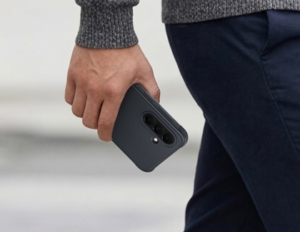 A person walking while holding a Galaxy A37 in a black rugged case with a textured back.