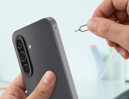 Hands holding a Galaxy A17 and using a metal SIM card ejection pin to open the SIM card tray on the side frame.