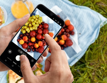 Person using two fingers to pinch and zoom on a photo of fruit displayed on a phone screen.