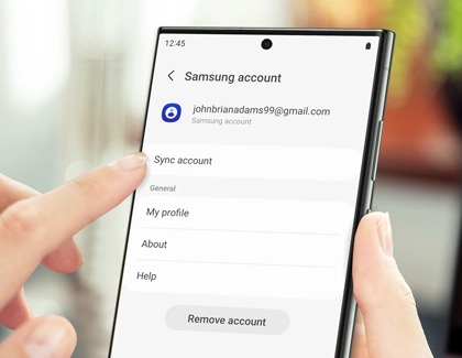 Hand holding a Galaxy S23 Ultra with a finger pointing to Sync account in Samsung account settings