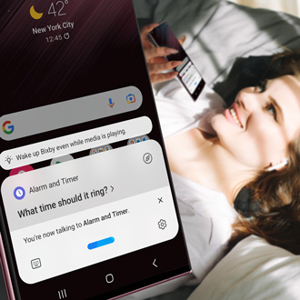 A woman using a Galaxy phone to set an alarm with Bixby while lying in bed