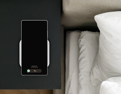 A Galaxy S25 phone placed on a wireless charging pad next to a bed.