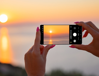 Person holding a Galaxy S25 Ultra capturing a sunset over water using the camera app.