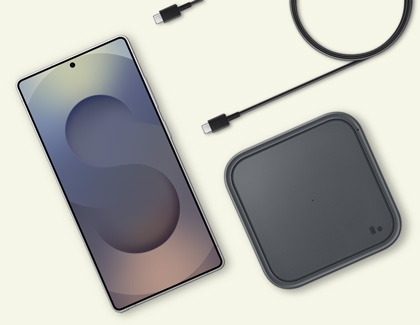 A Galaxy S25 phone next to a wireless charging pad and a USB cable.
